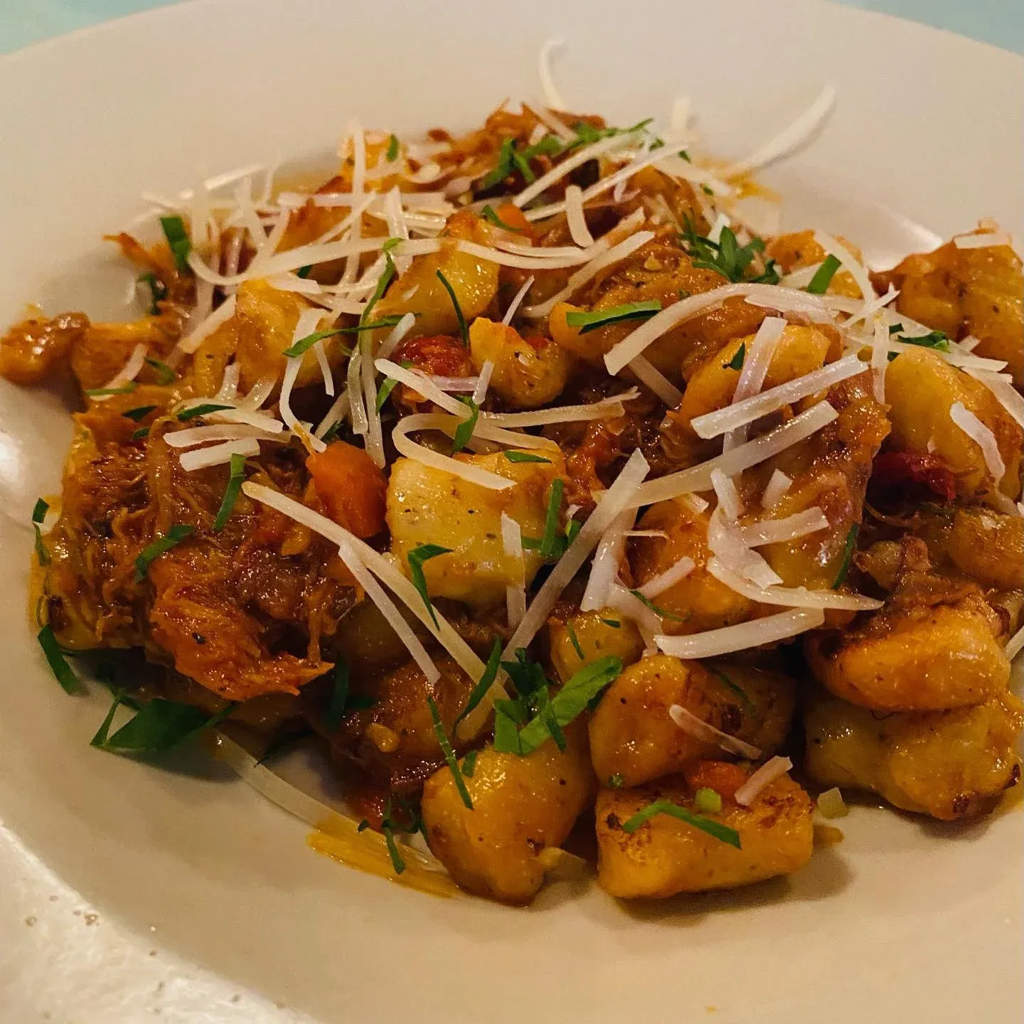 Gnocchi with meat sauce, shredded cheese, and herbs in a white bowl.