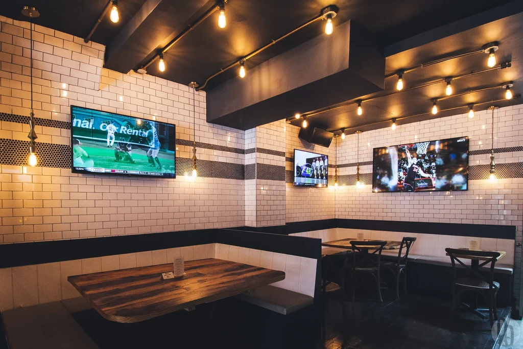 A restaurant interior with multiple TVs showing sports, booths, and Edison bulbs.