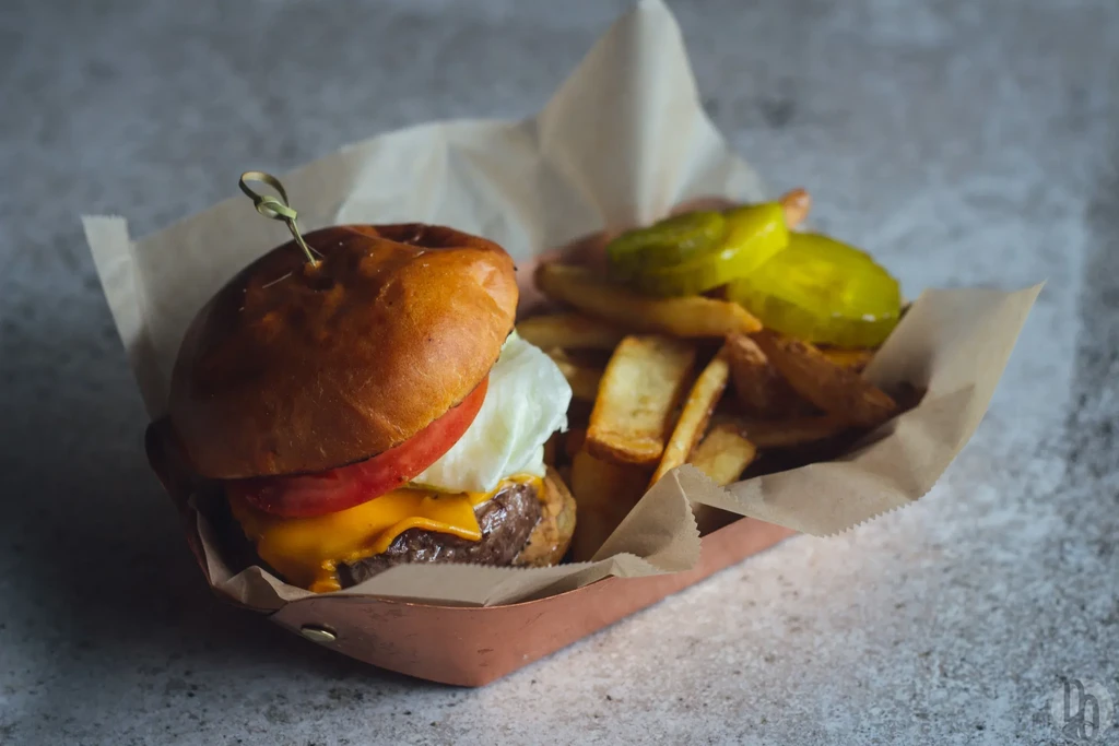 A cheeseburger, fries, and pickles served in a copper basket.