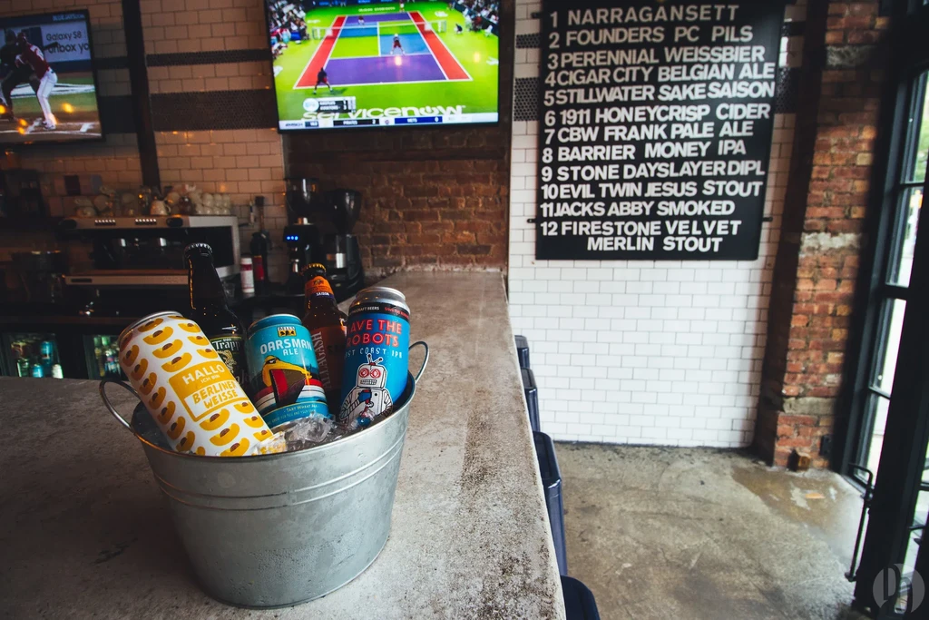A bucket of beer cans on a bar with a menu and TV.