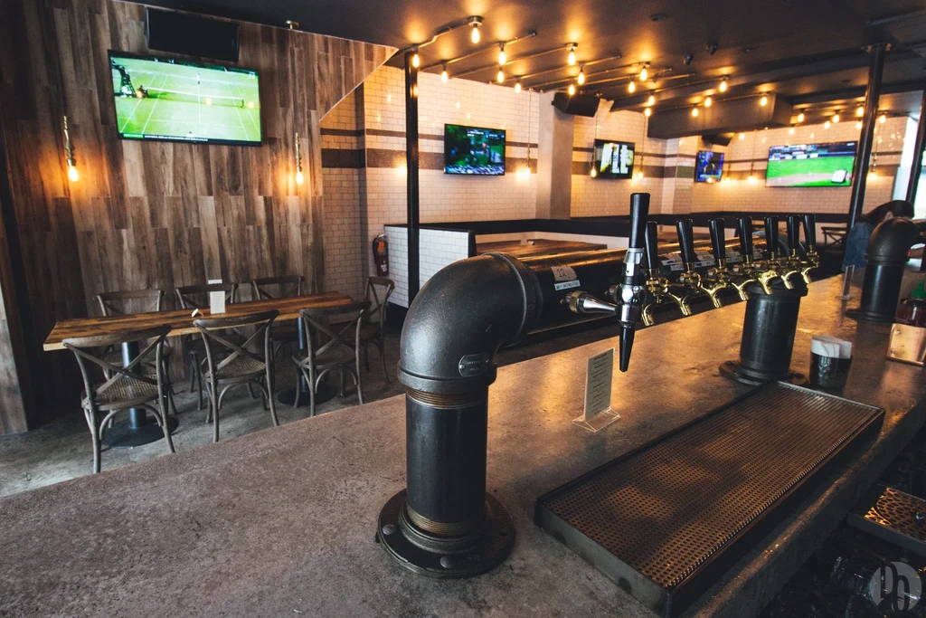An empty bar area with beer taps, tables, chairs, and TVs.