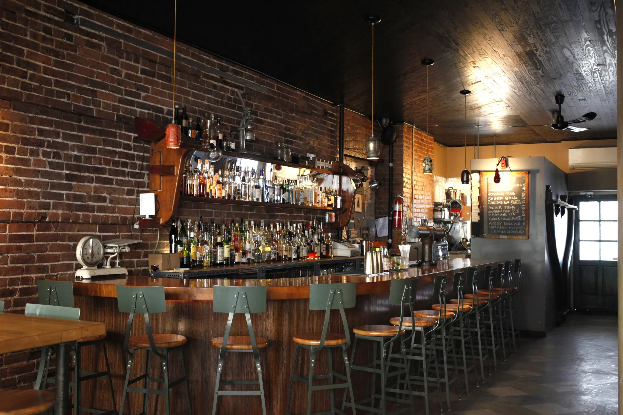 Interior of a bar with brick walls, wooden counter, and bar stools.