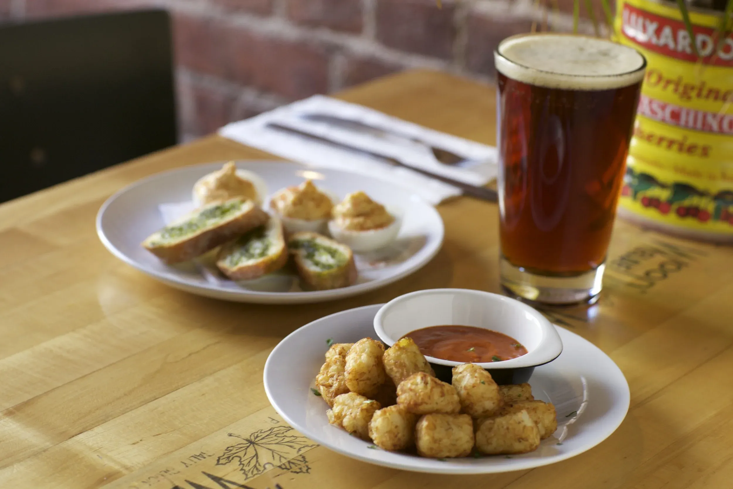 Plates of tater tots and deviled eggs, a beer, on a wooden table.
