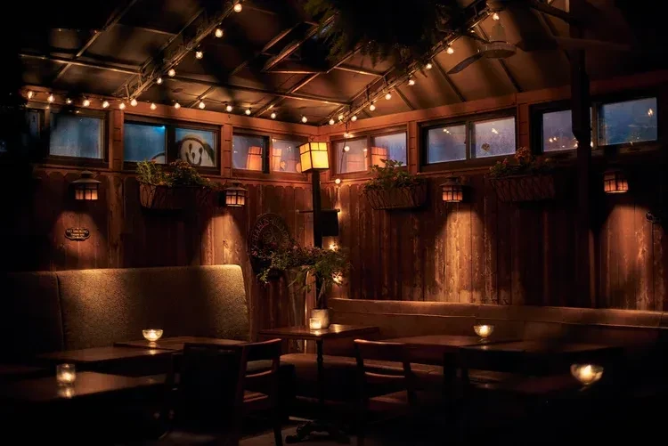 An empty, cozy wooden restaurant interior with warm lighting and a sloped ceiling.