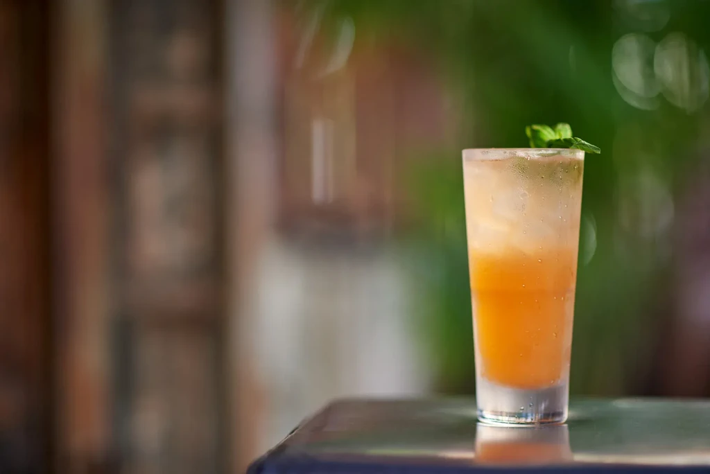 A tall glass with an orange drink and mint on a table.