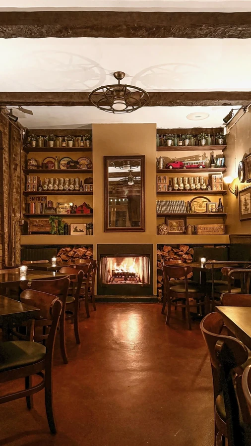 Warmly lit dining room with fireplace, wooden shelves, and exposed ceiling beams.