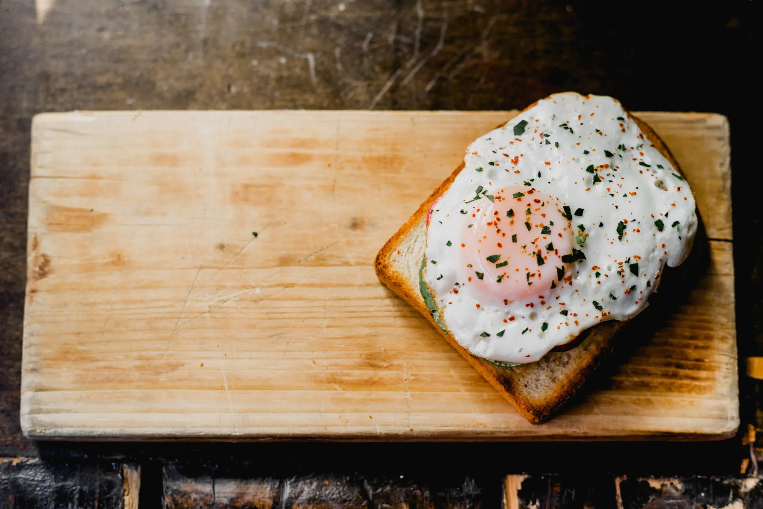 Sunny-side up egg on toast, garnished with herbs and chili flakes.