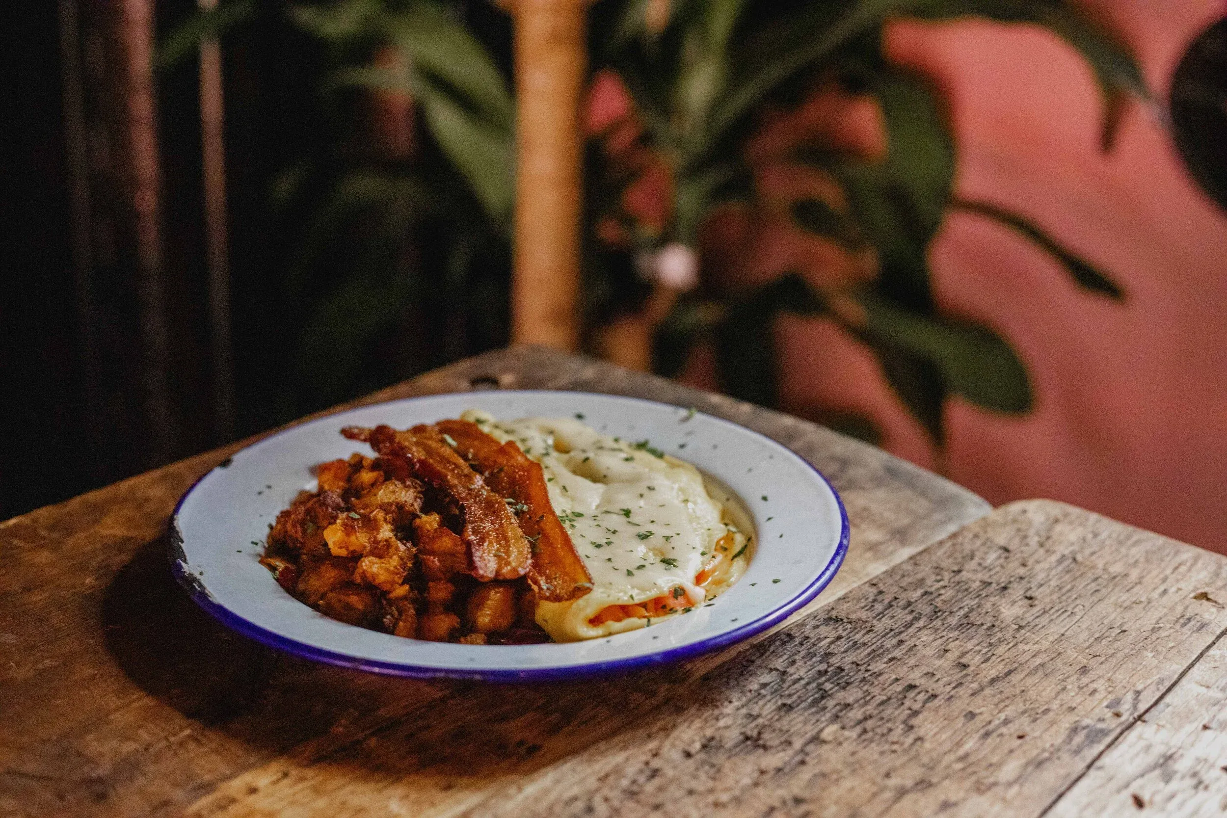 A plate of bacon, potatoes, and lasagna on a wooden table.