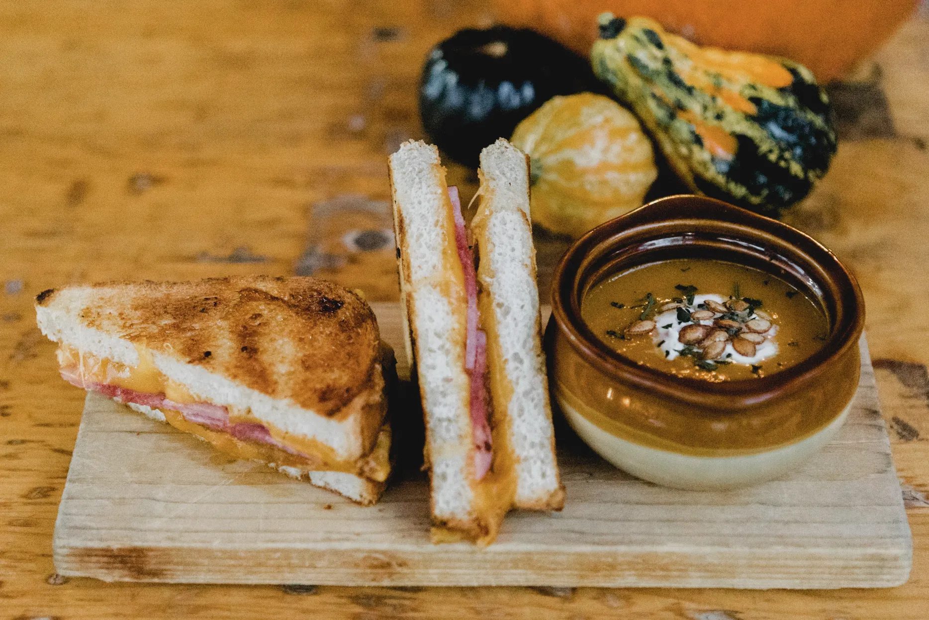 Grilled cheese and ham sandwich with soup on a wooden board.