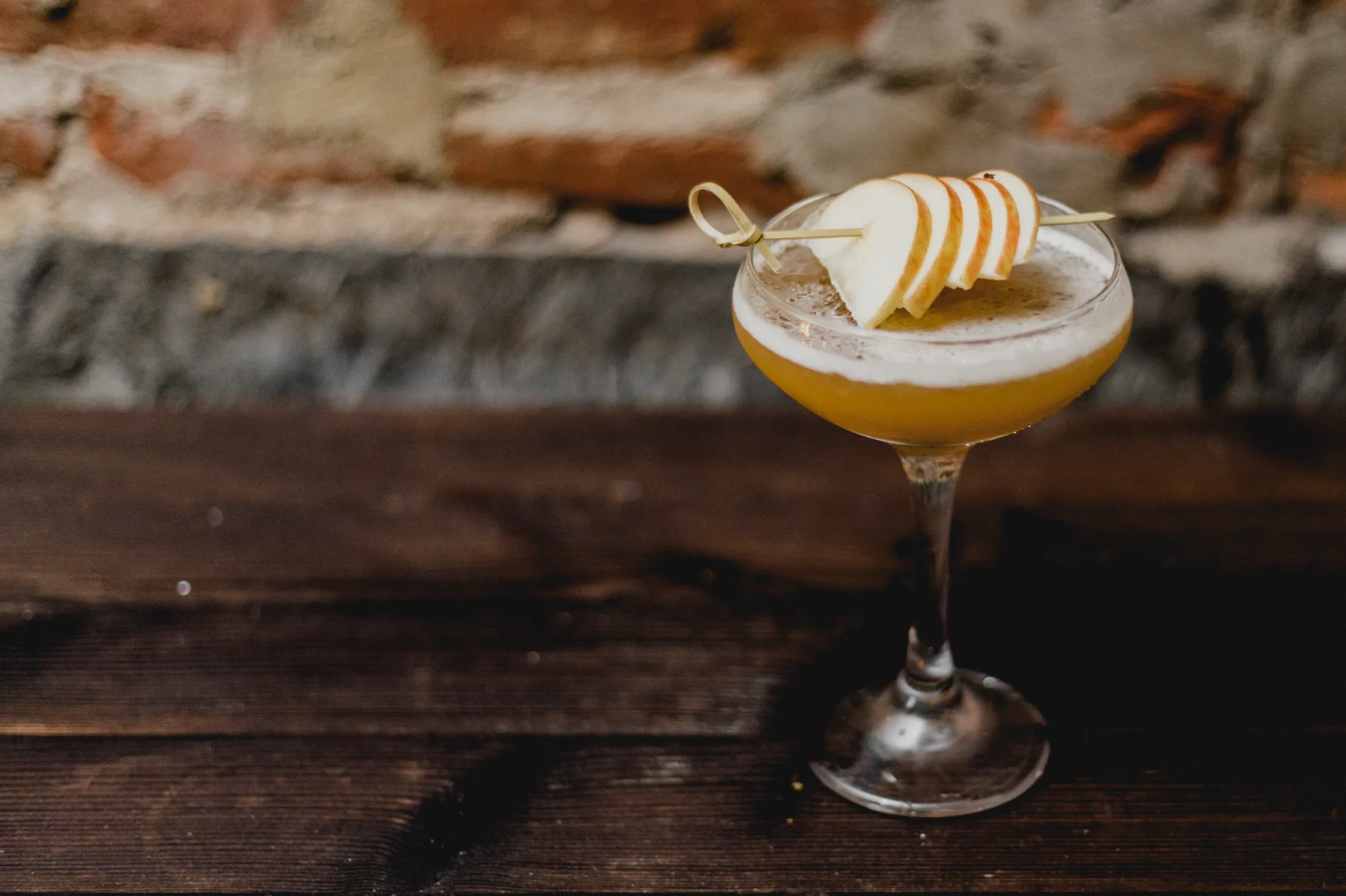 Cocktail in a coupe glass garnished with apple slices on a wooden table.