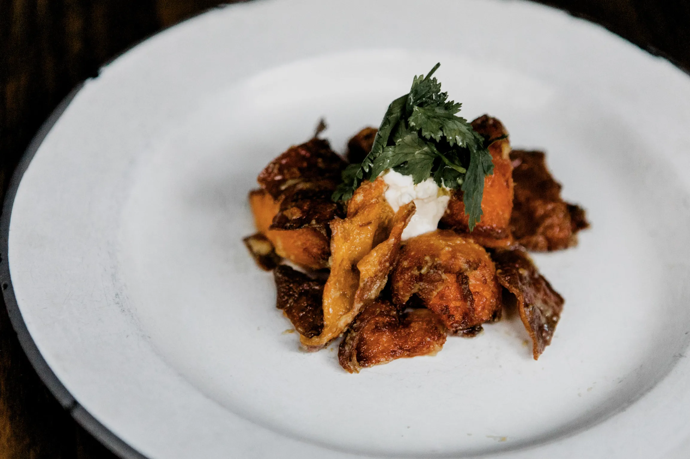Crispy roasted squash with creamy topping and fresh cilantro on a white plate.