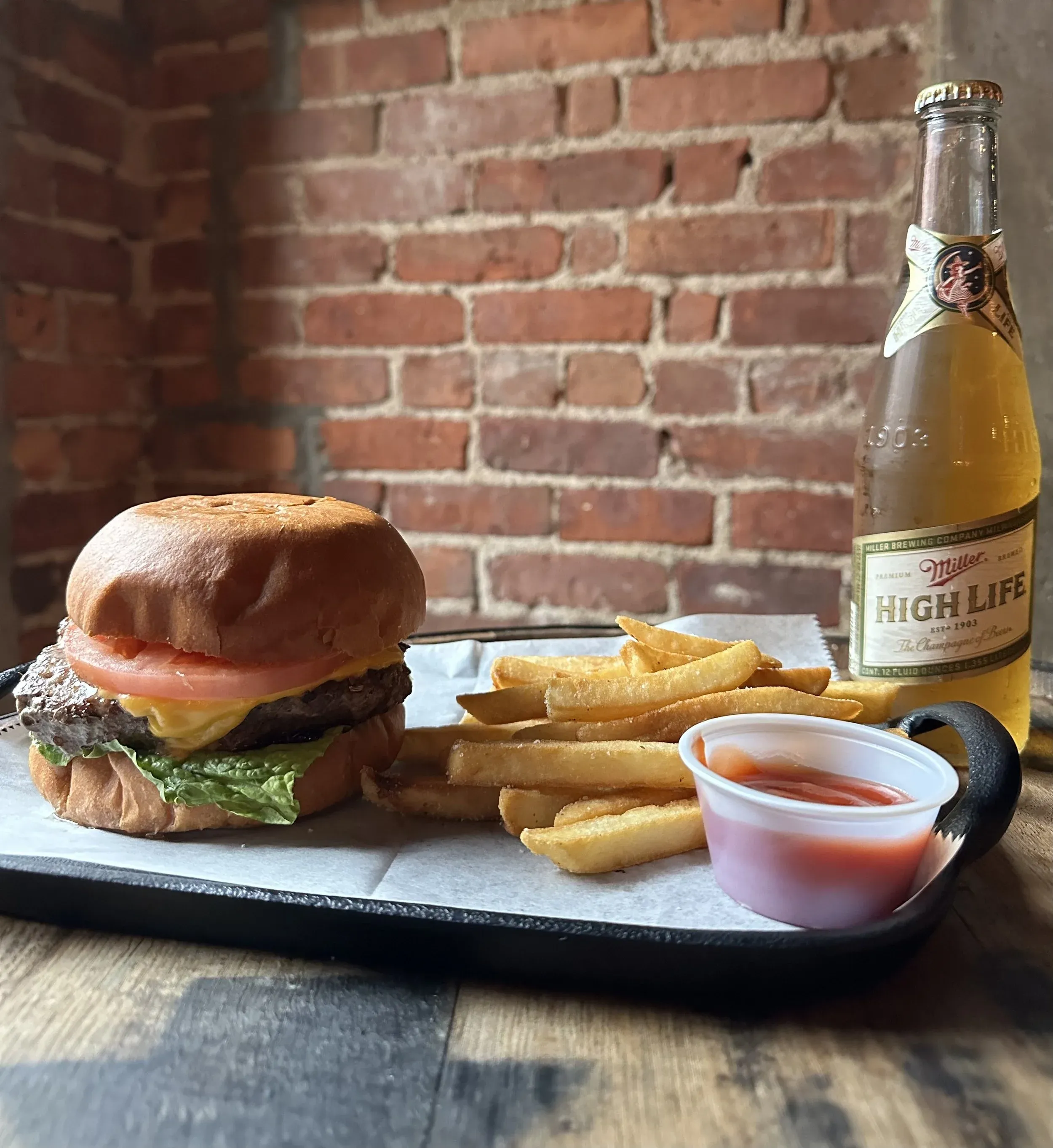 Cheeseburger, french fries, ketchup, and Miller High Life on a tray.