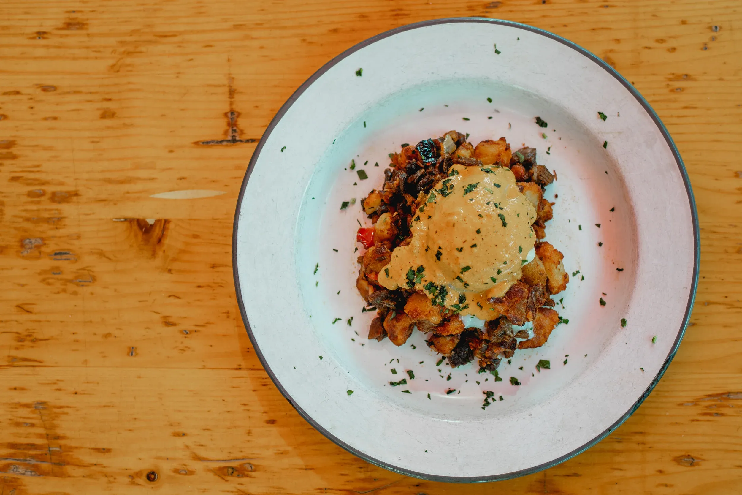 A plate of breakfast potatoes topped with a poached egg and sauce.