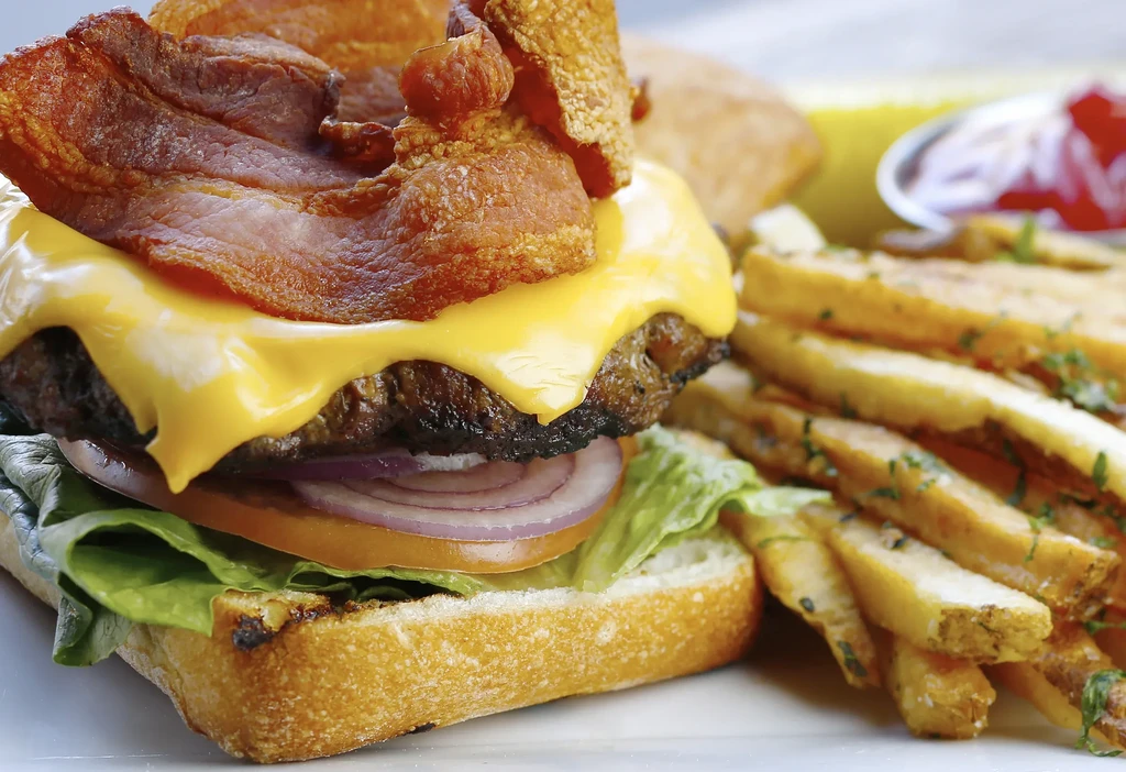 A cheeseburger with bacon, lettuce, onion, tomato, and french fries.