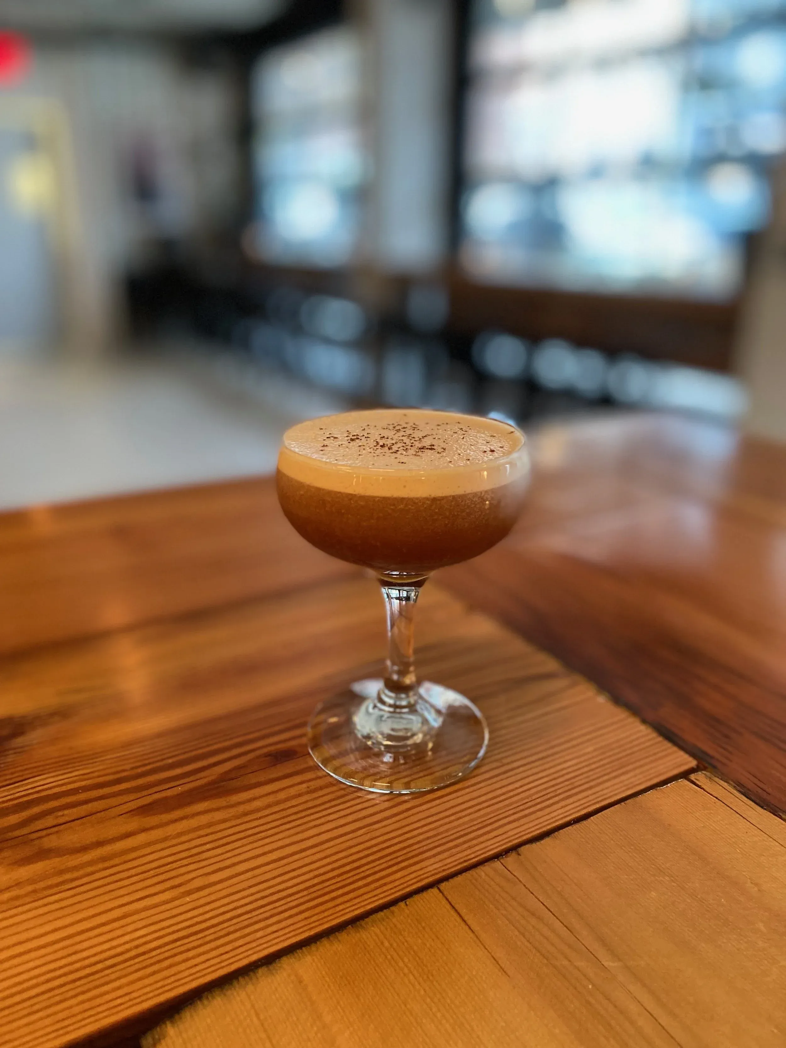 An espresso martini with foam and cocoa powder on a wooden table.