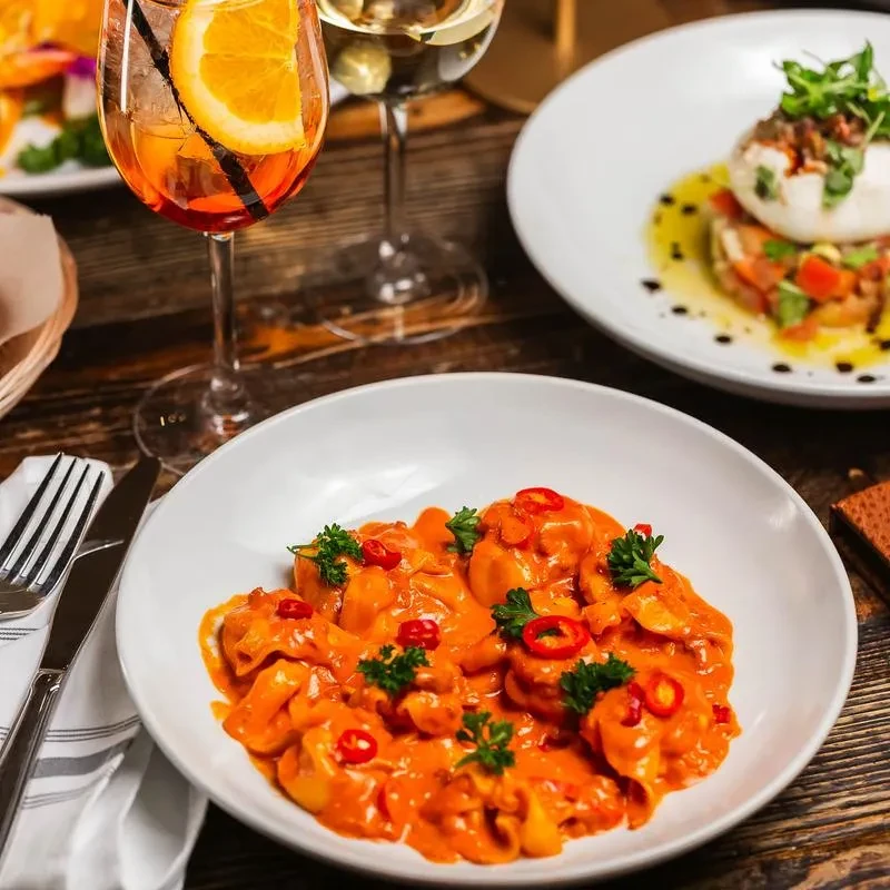 Pasta in red sauce with peppers, drinks, and another dish on a table.