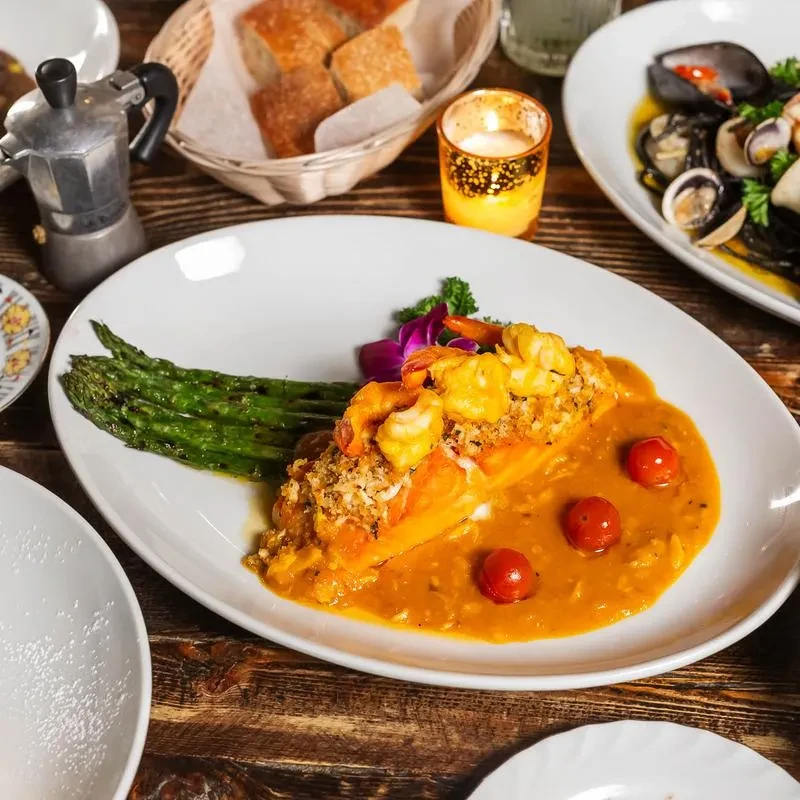 Salmon with shrimp, asparagus, sauce, and cherry tomatoes on a plate.