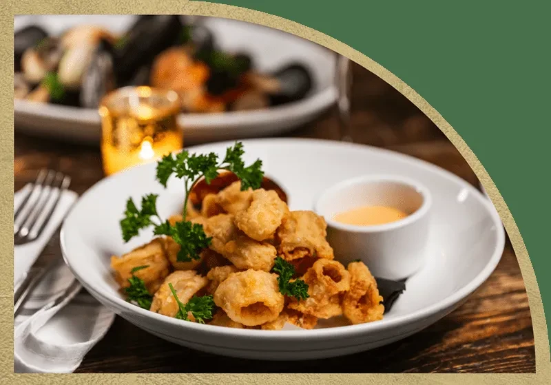 Fried calamari with parsley garnish and dipping sauce on a white plate.