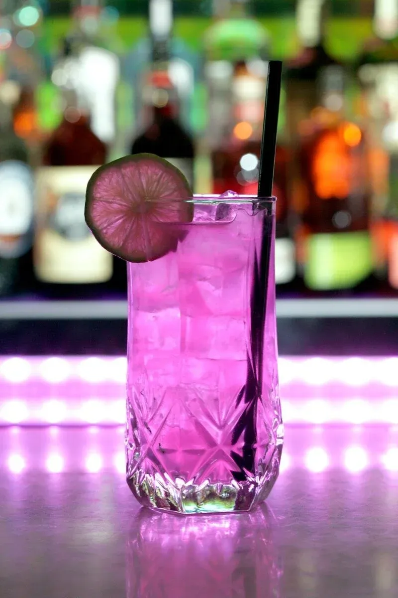 A tall glass with a pink drink, ice, a lime slice, and a straw.