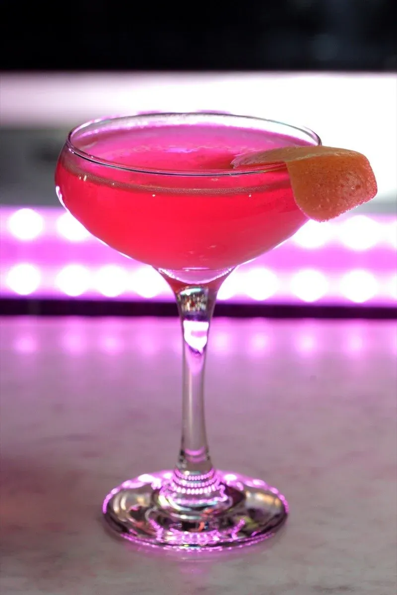 Pink cocktail in a coupe glass with an orange peel garnish.