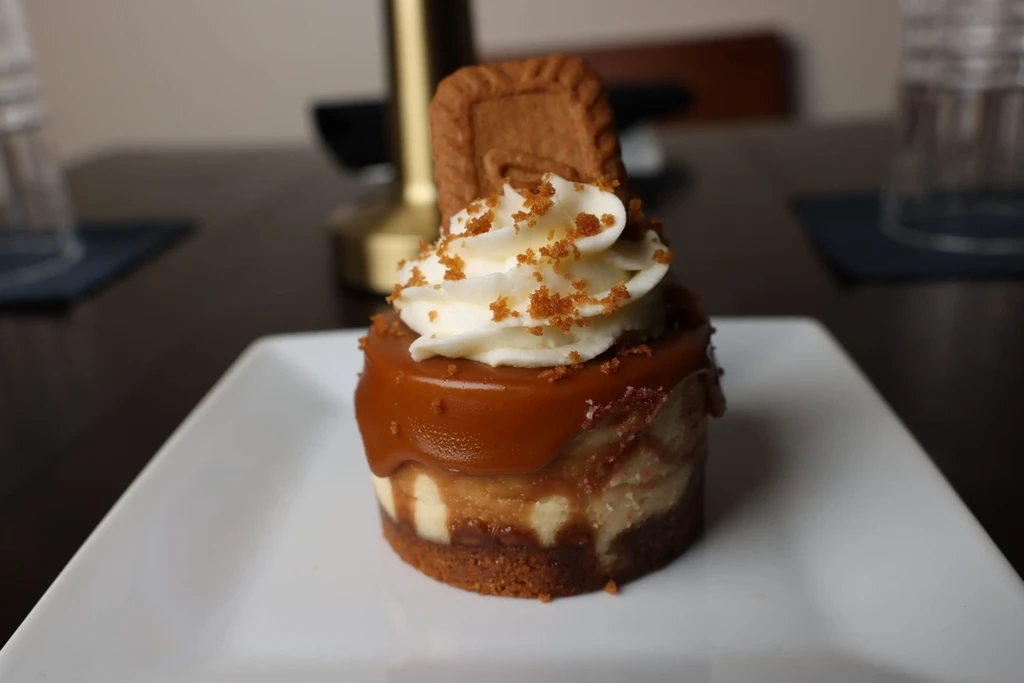 Miniature cheesecake topped with caramel, whipped cream, and a Biscoff cookie.