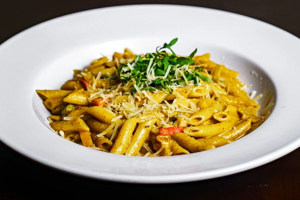 Penne pasta with sauce, cheese, and herbs in a white bowl.