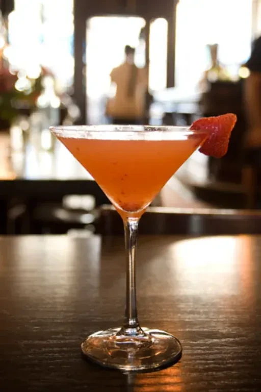 Pink martini with strawberry garnish on a dark wooden table.