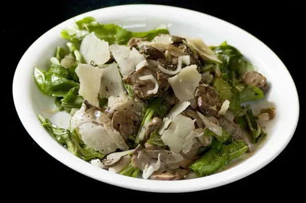 A white bowl of salad with greens, mushrooms, and cheese.