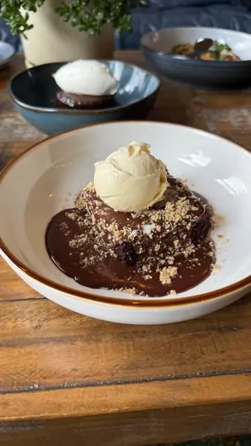 Brownie with chocolate sauce, crushed nuts, and vanilla ice cream in a white bowl.