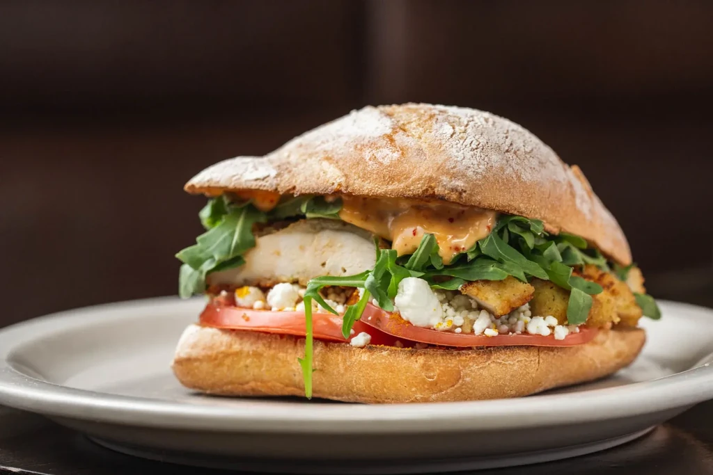 A chicken sandwich with arugula, tomatoes, and cheese on a bun.