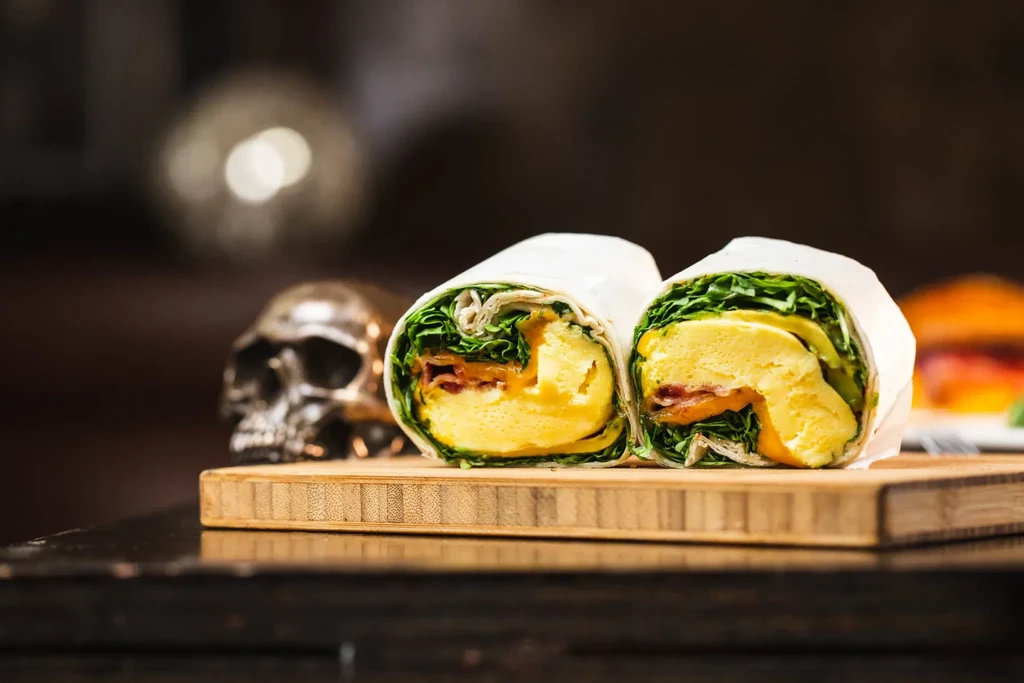 Two halves of an egg and bacon wrap on a wooden board.