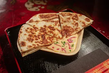 Flatbread cut into wedges, with a dipping sauce, on a black tray.