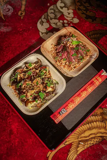 Two meals and chopsticks on a black tray with a red background.