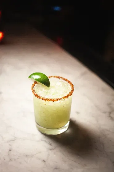 A pale green drink with a chili-salt rim and a lime wedge.