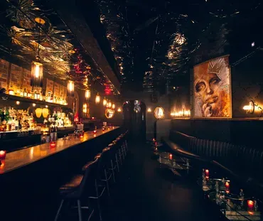 Dark, moody bar interior with long bar, booths, and large artwork.