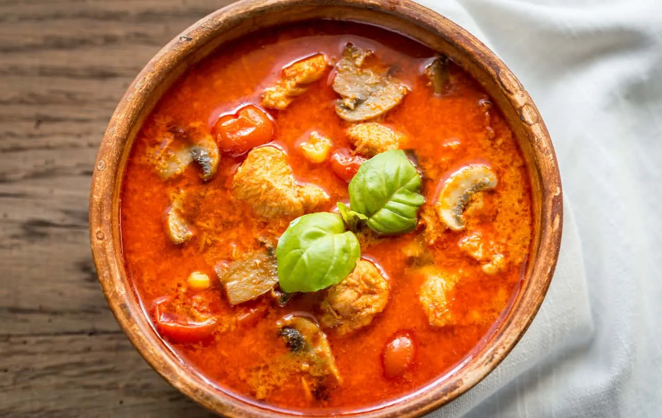 Overhead shot of a rustic bowl of red curry with basil.