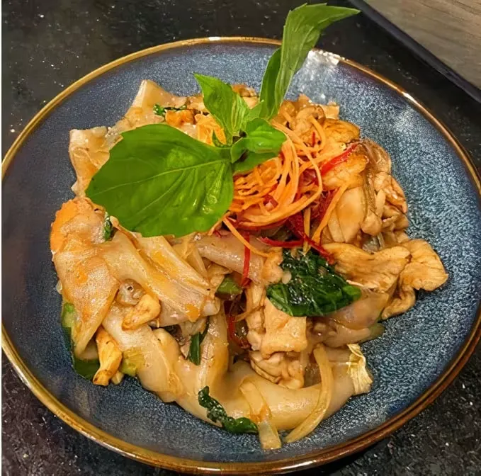 Stir-fried chicken and noodles with basil on a blue plate.