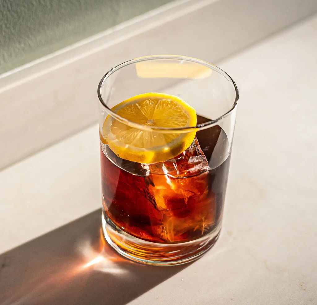 Dark beverage with ice and a lemon slice in a glass.