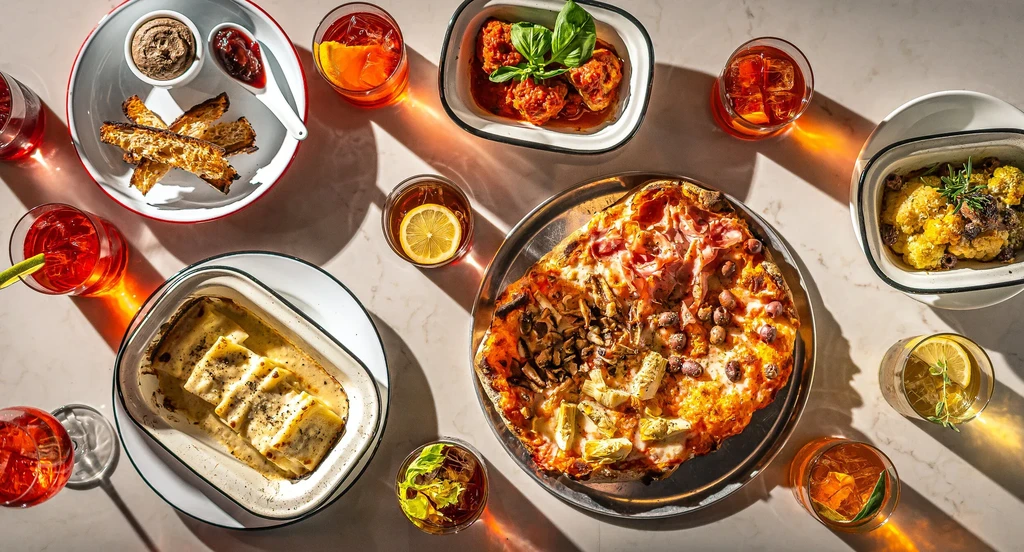 Overhead view of a feast with pizza, pasta, meats, and cocktails.