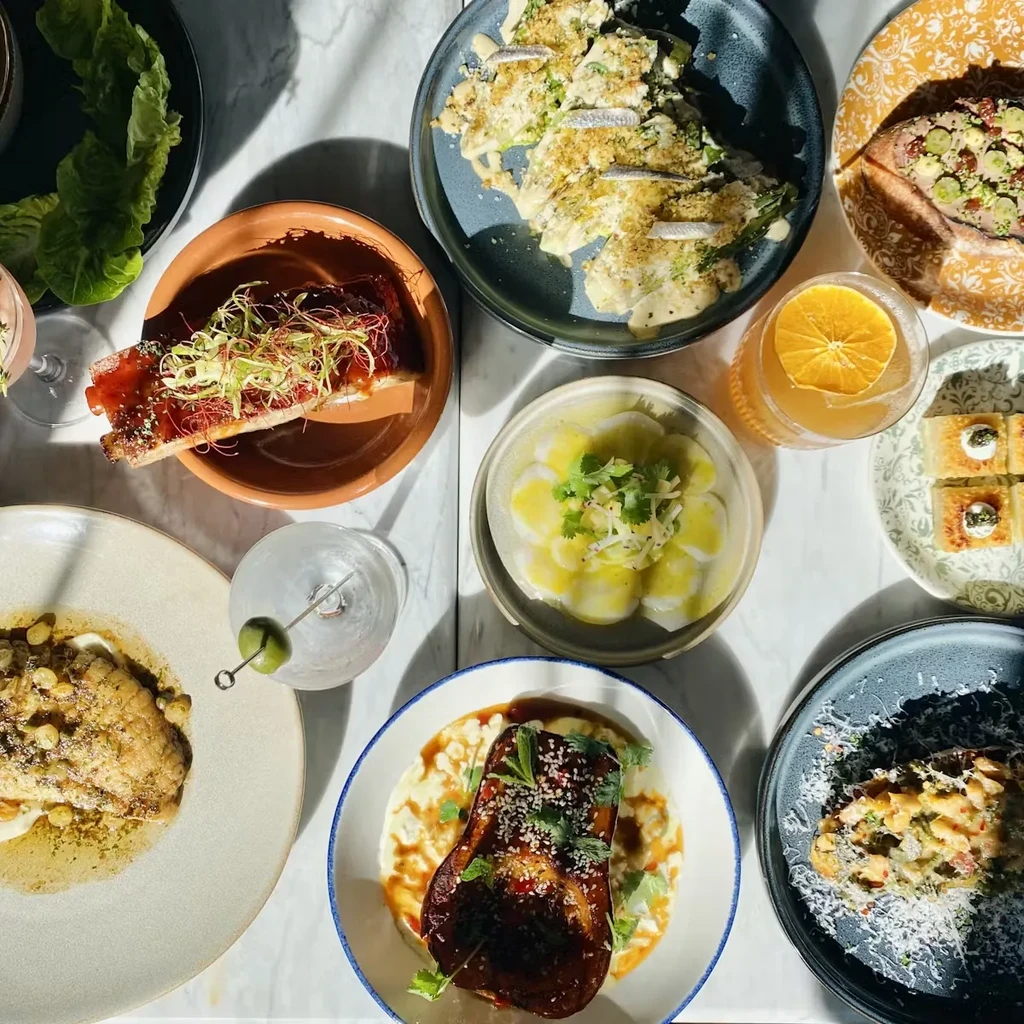 An overhead view of a table laden with several plates of food and drinks.