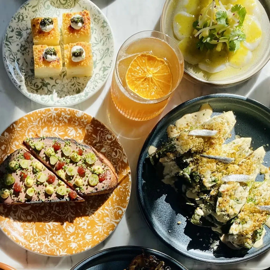 An overhead shot of several appetizer plates and a cocktail on a table.
