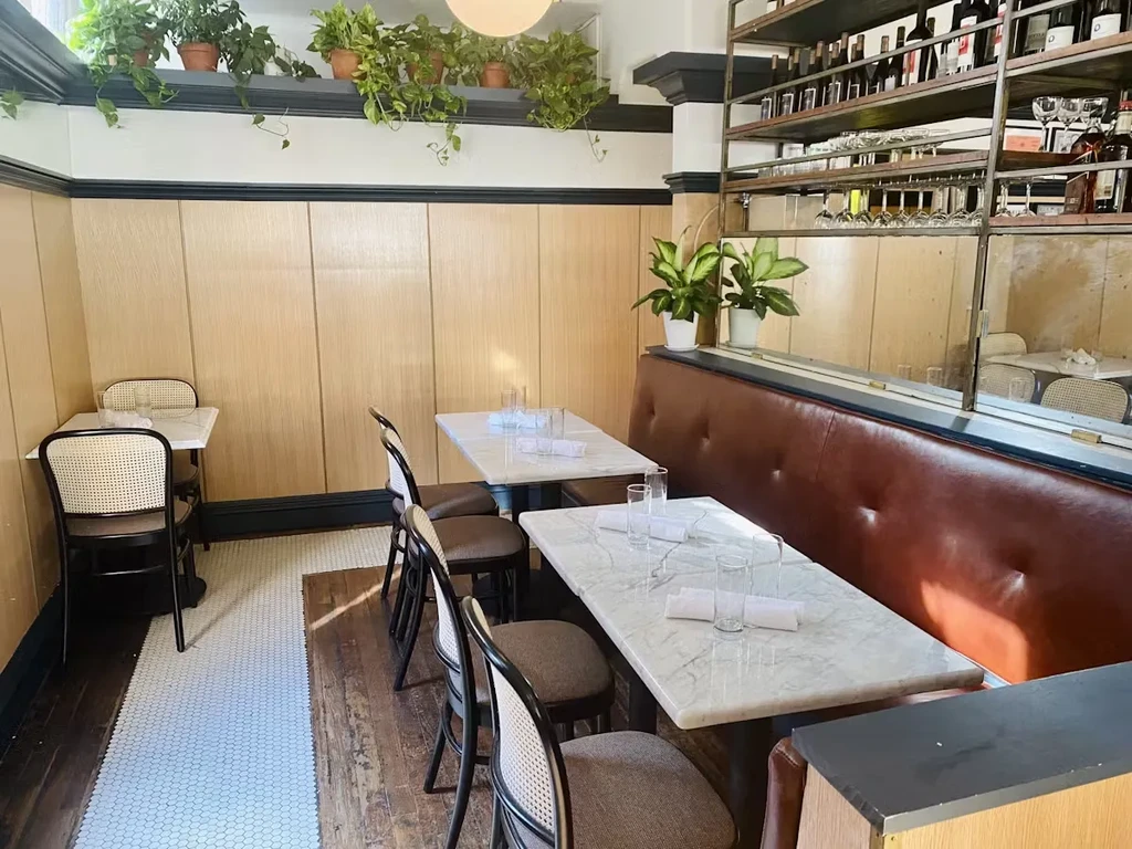Empty restaurant interior with marble tables, brown booths, and potted plants.