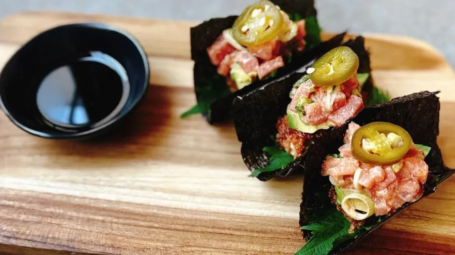 Three tuna avocado seaweed bites topped with jalapeño, with a sauce bowl.