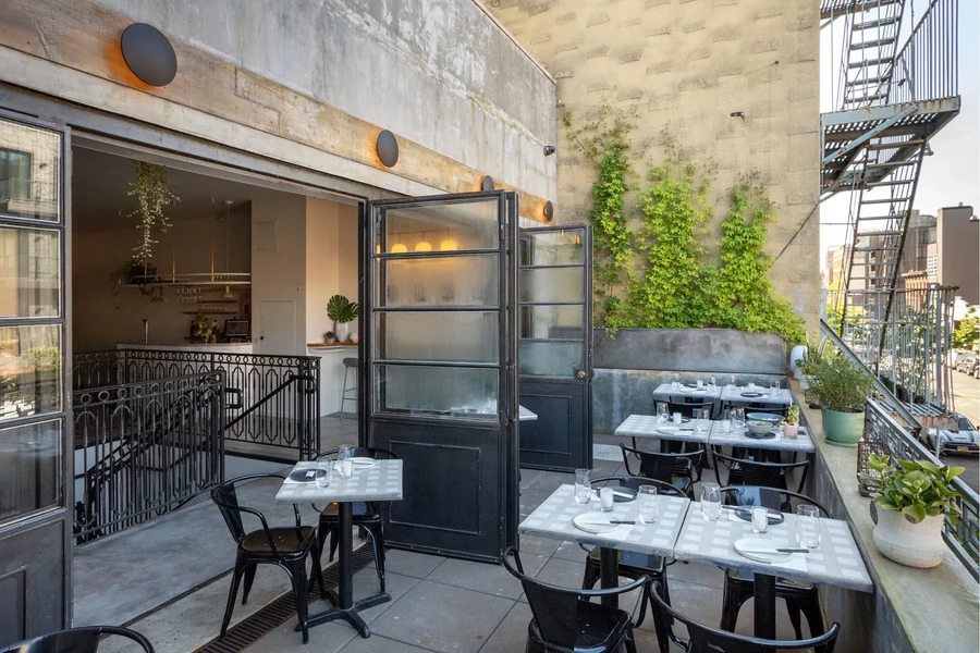 Outdoor restaurant patio with tables, green vines, and a fire escape.