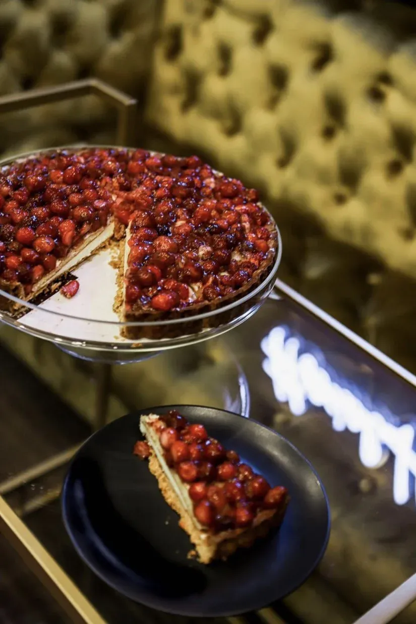 Glazed strawberry tart on cake stand, slice on black plate.