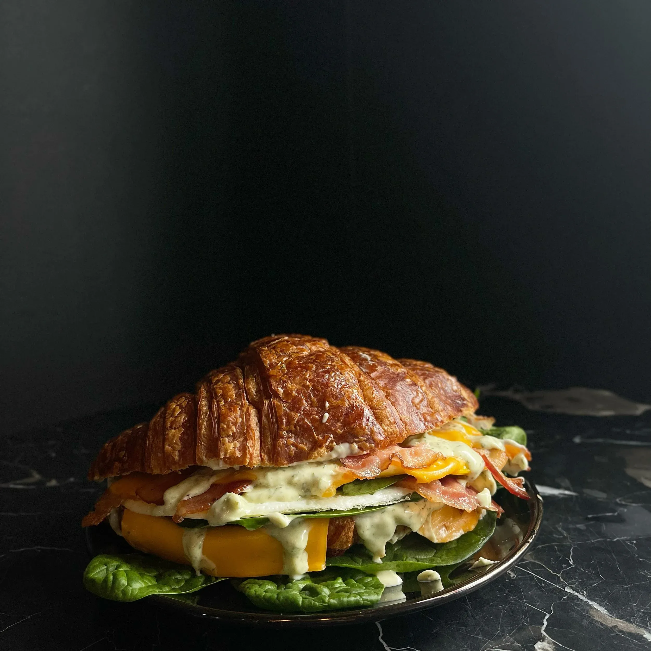 Croissant sandwich with bacon, egg, cheese, spinach, and a creamy sauce.