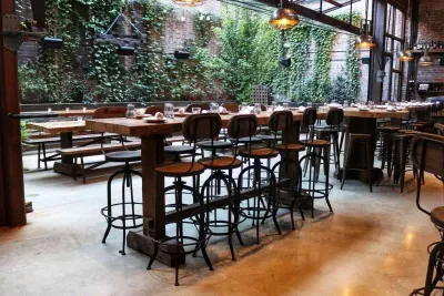 An empty restaurant patio with high-top tables, bar stools, and lush green vines.