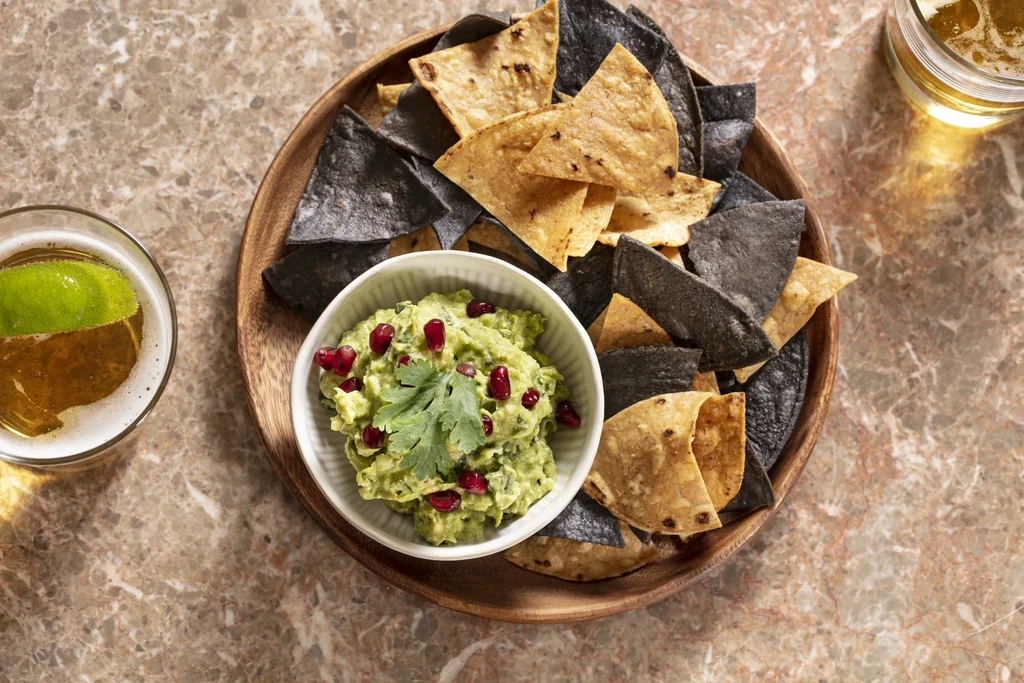 Guacamole with tortilla chips and two beers on a marble table.