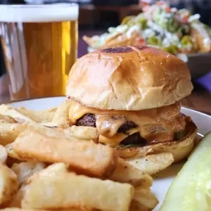 A cheeseburger and fries with a beer and salad in the background.
