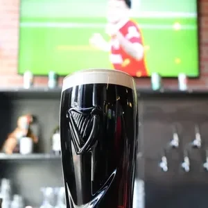 A full glass of Guinness in front of a TV showing soccer.